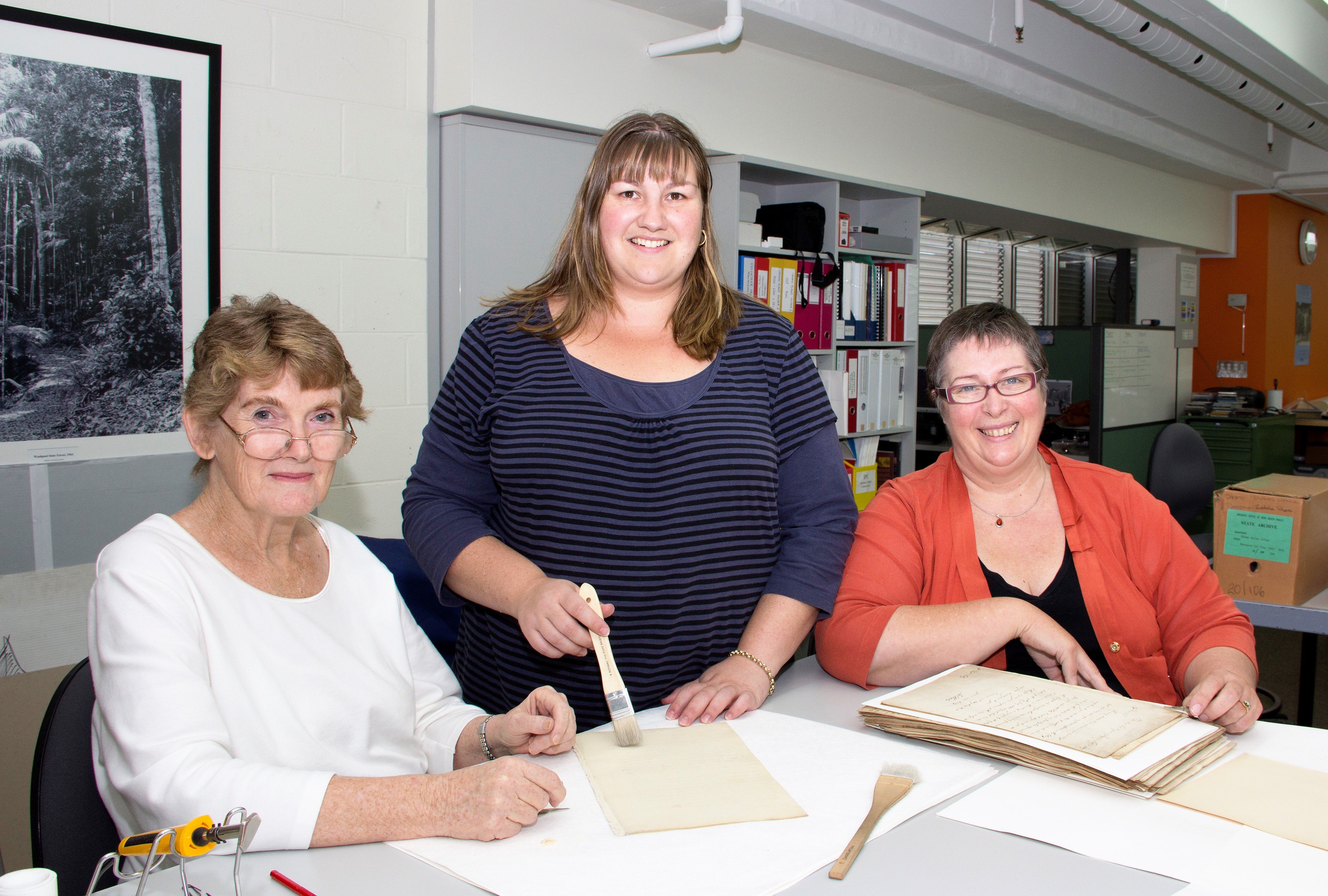 Three women at a work table with a bundles of archival papers