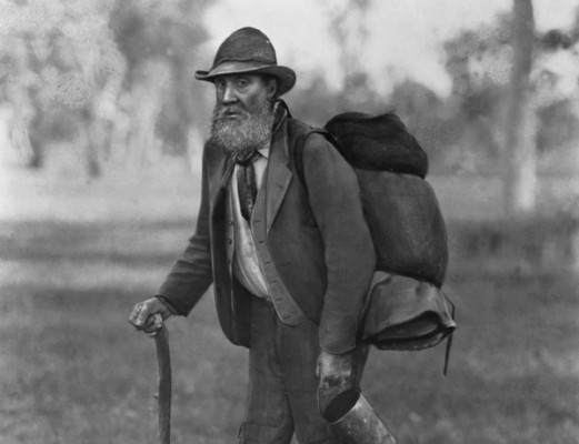 A swagman with a backpack uses a walking stick and holds a tin can