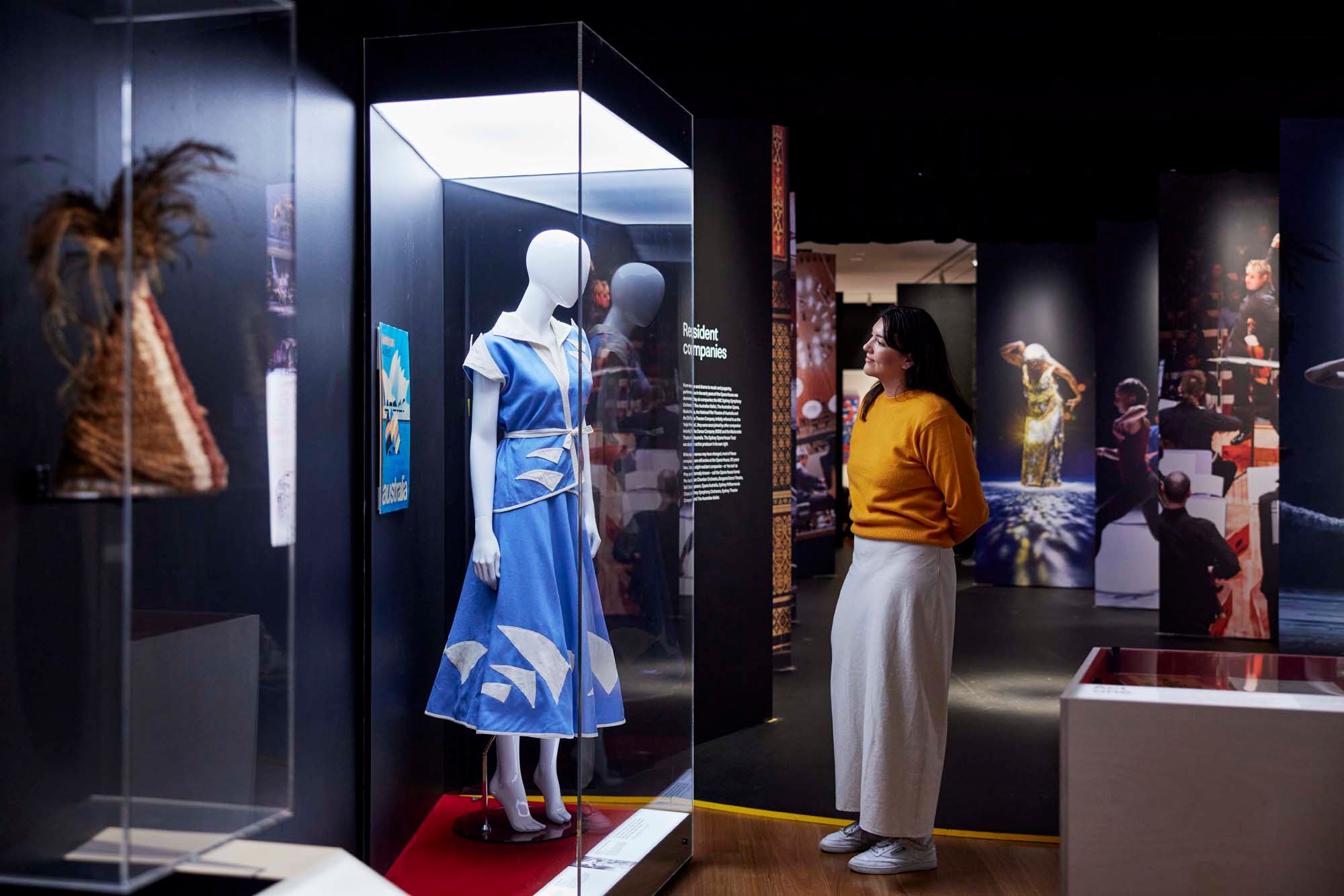 A woman browses an exhibition display of a mannequin wearing a blue dress imprinted with the sails of the Sydney Opera House