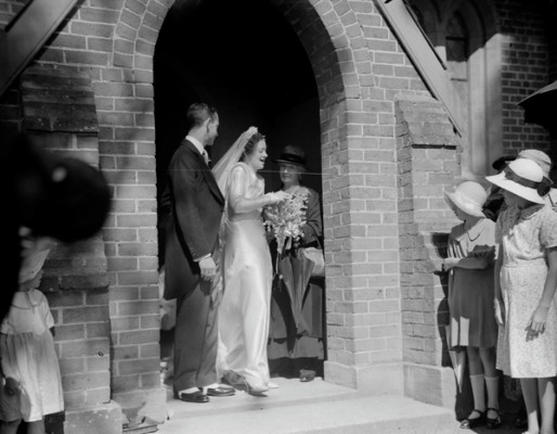 A bride and groom leave church as well wishers look on