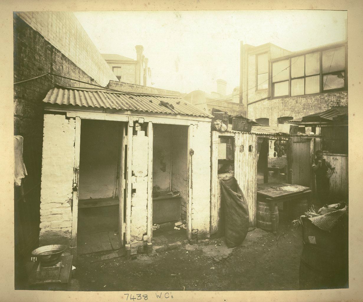 A rundown shed of two toilet blocks stand next to the rear open workspace of a butcher