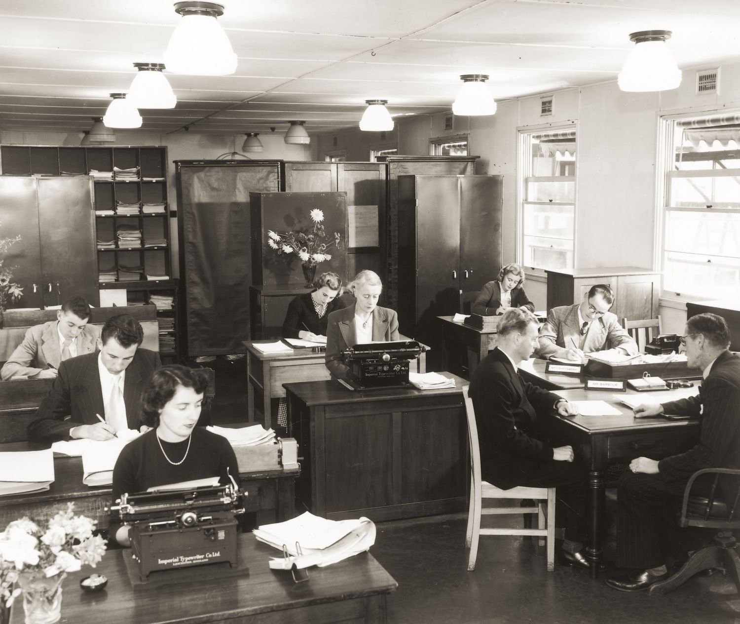 Black and white photo of a grou of people sitting at desks with type writers