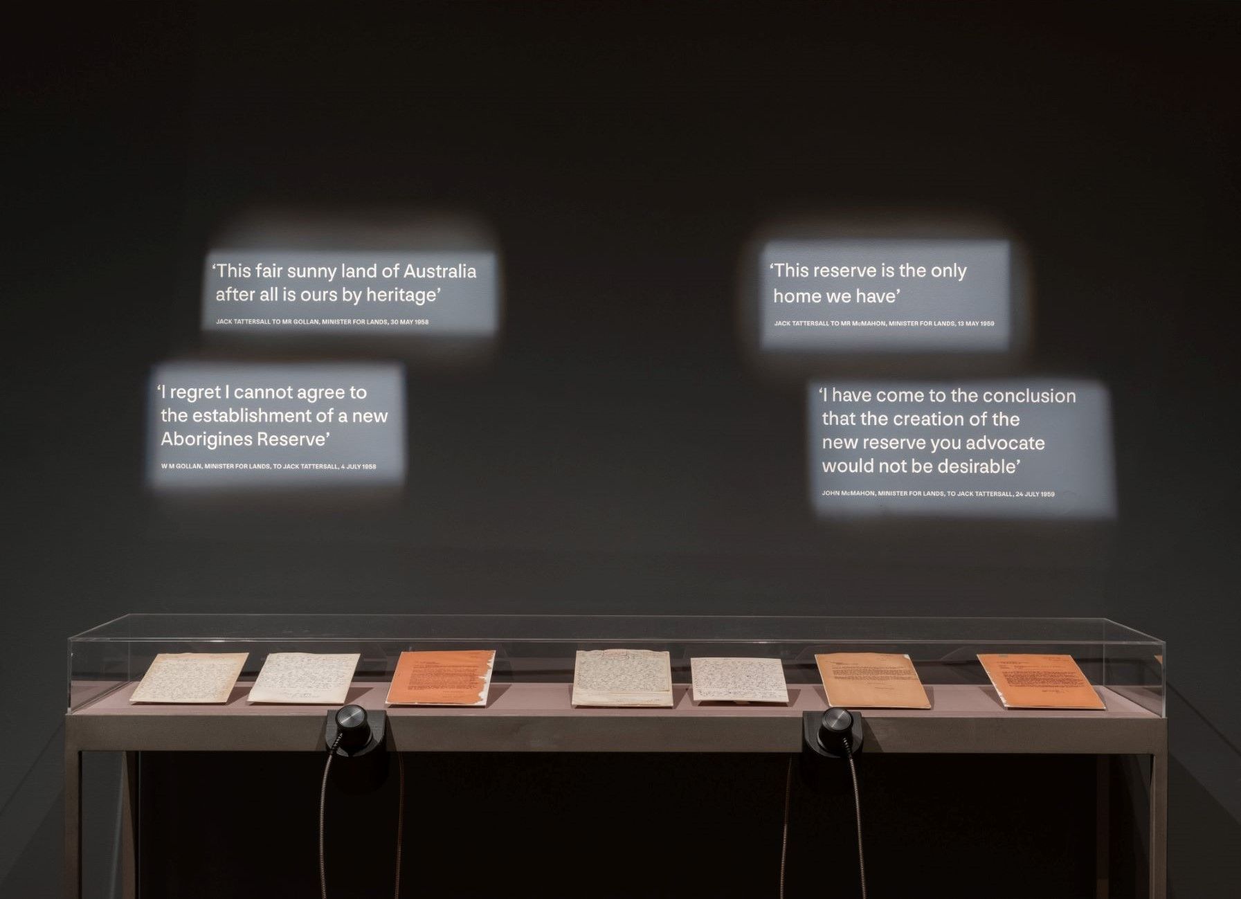 Lit text on black wall with letters in a glass display cabinet underneath