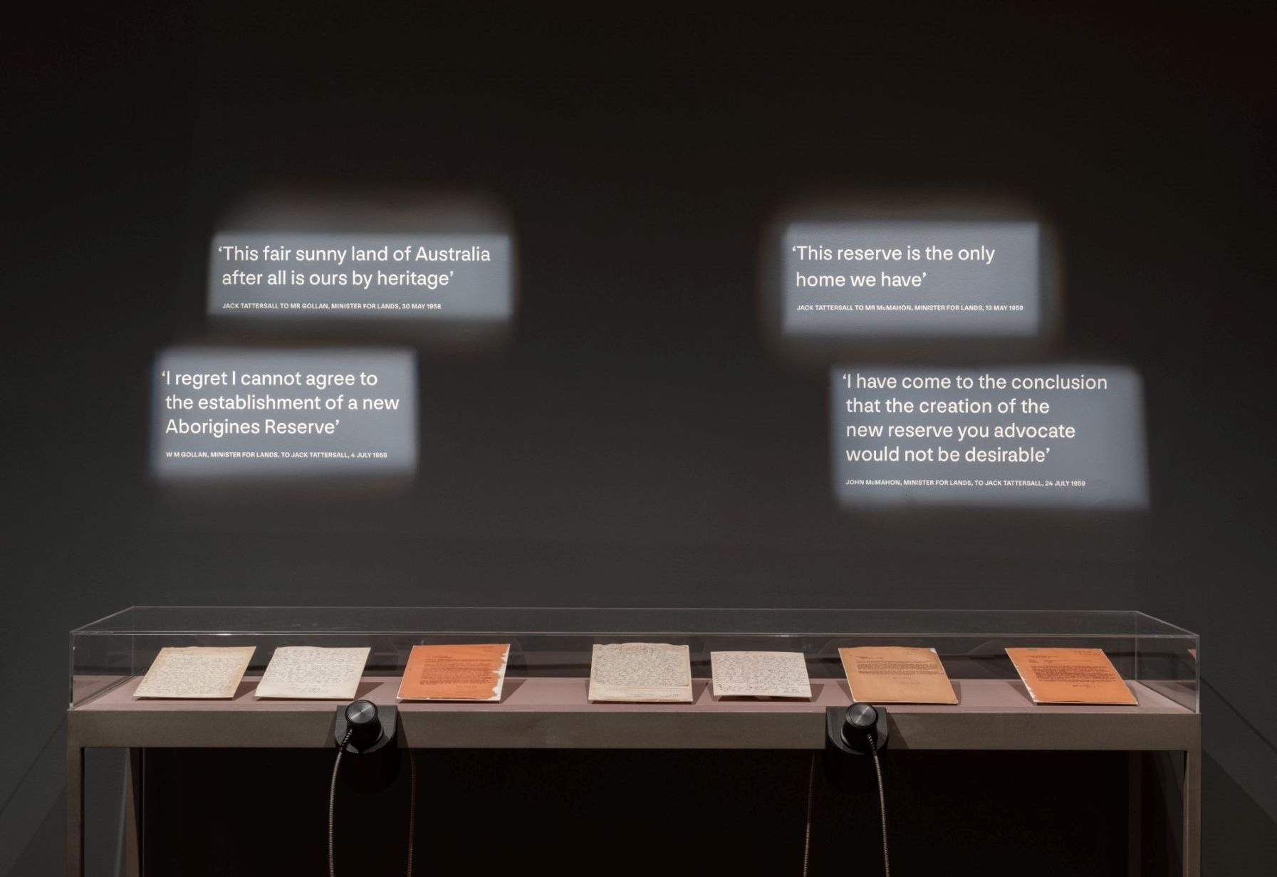 Lit text on black wall with letters in a glass display cabinet underneath