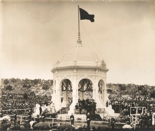A flag flies atop the Federation Pavilion at Centennial Park and a crowd of spectators watch the ceremony