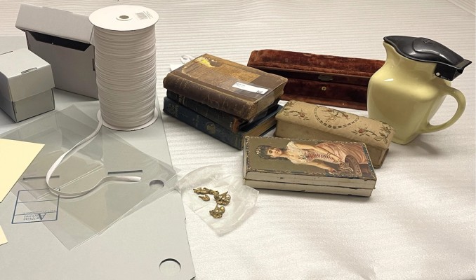 Objects from a collection sit next to archival storage boxes