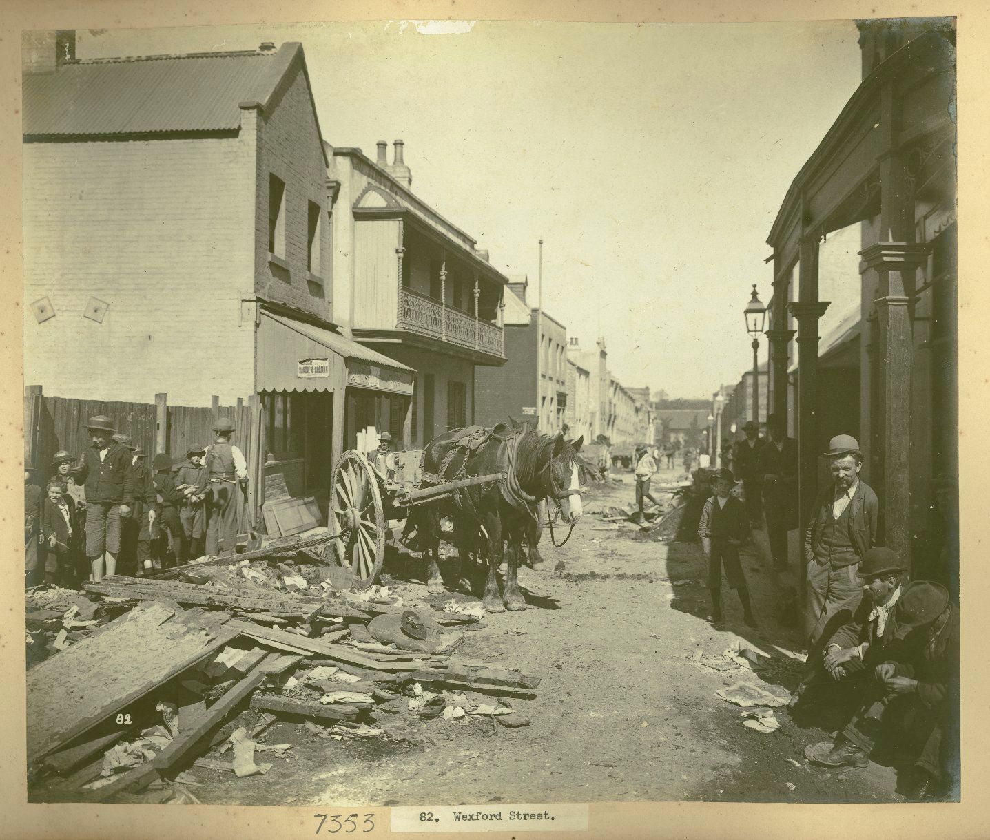 People pose casually along a dirt road. A horse and cart stand behind rubble that is piled on the street 