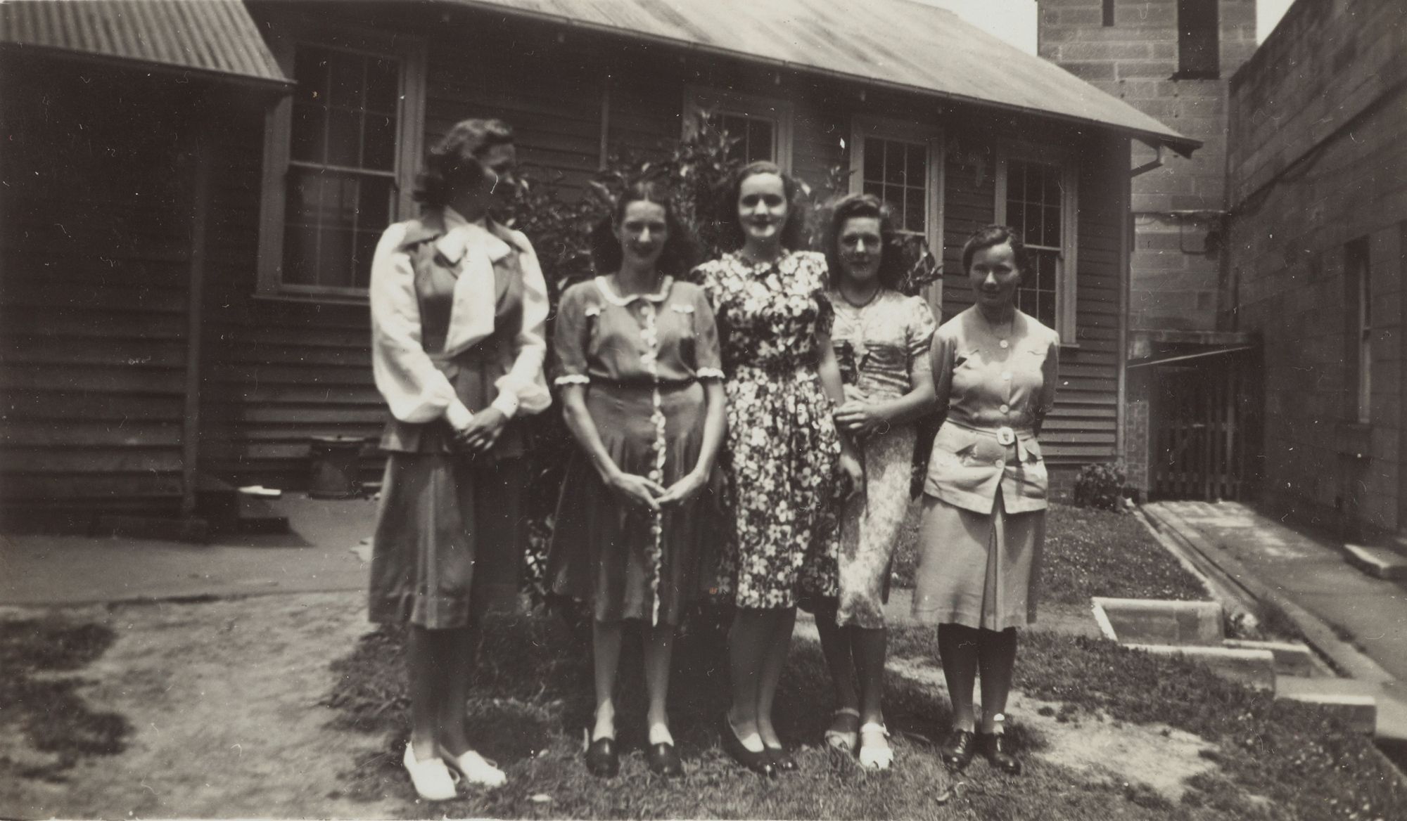Five women pose together in front of a wooden building