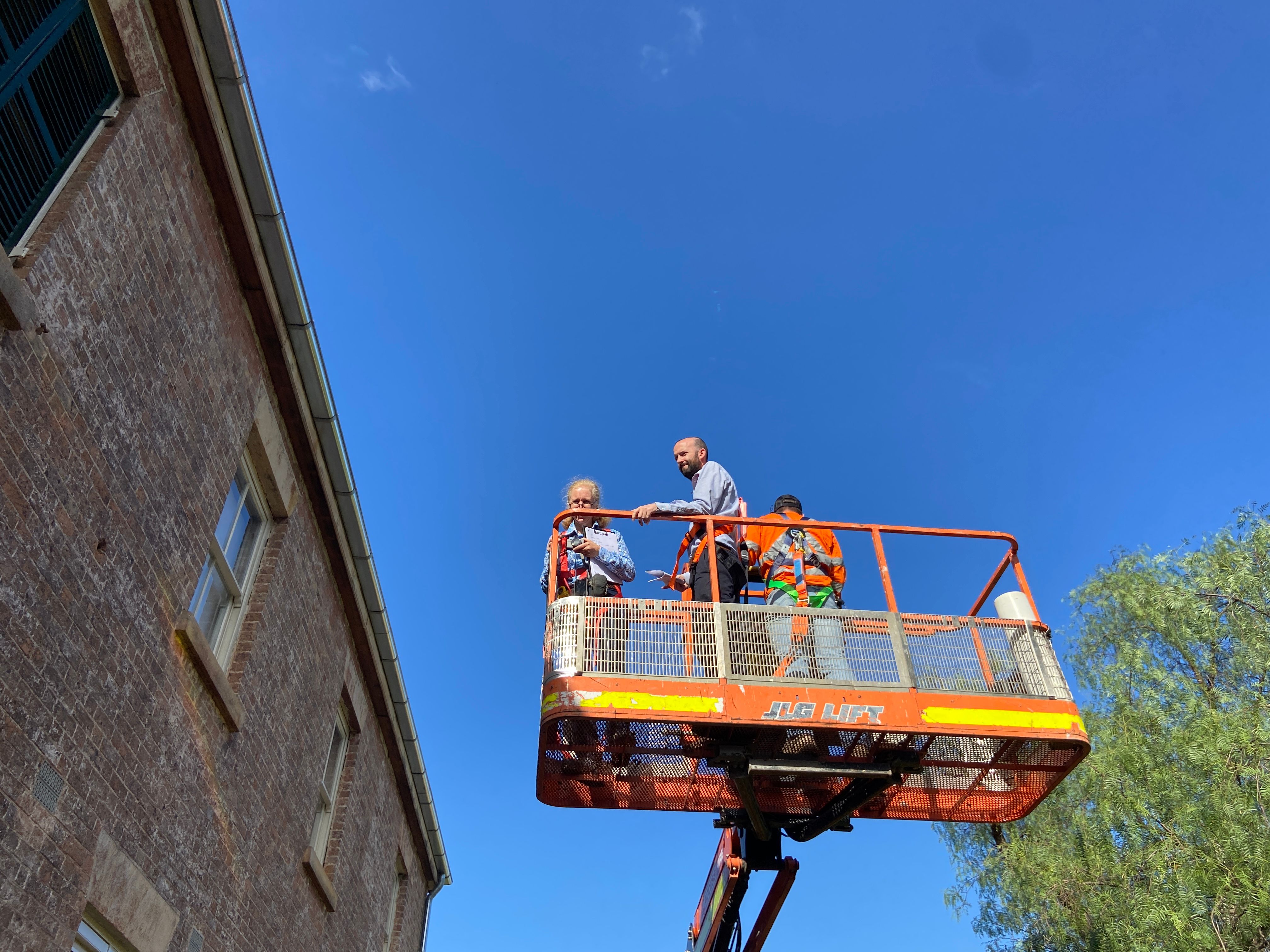 Group of people standing on a crane inspecting a roof