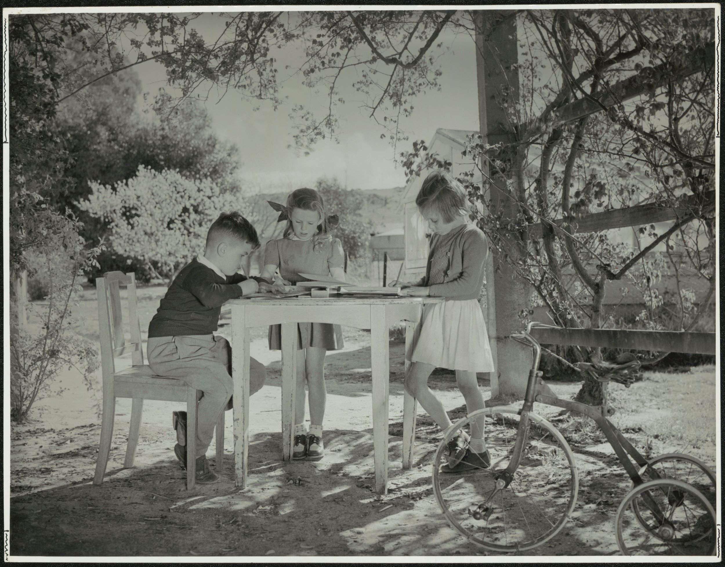 Three children study at a table outdoors
