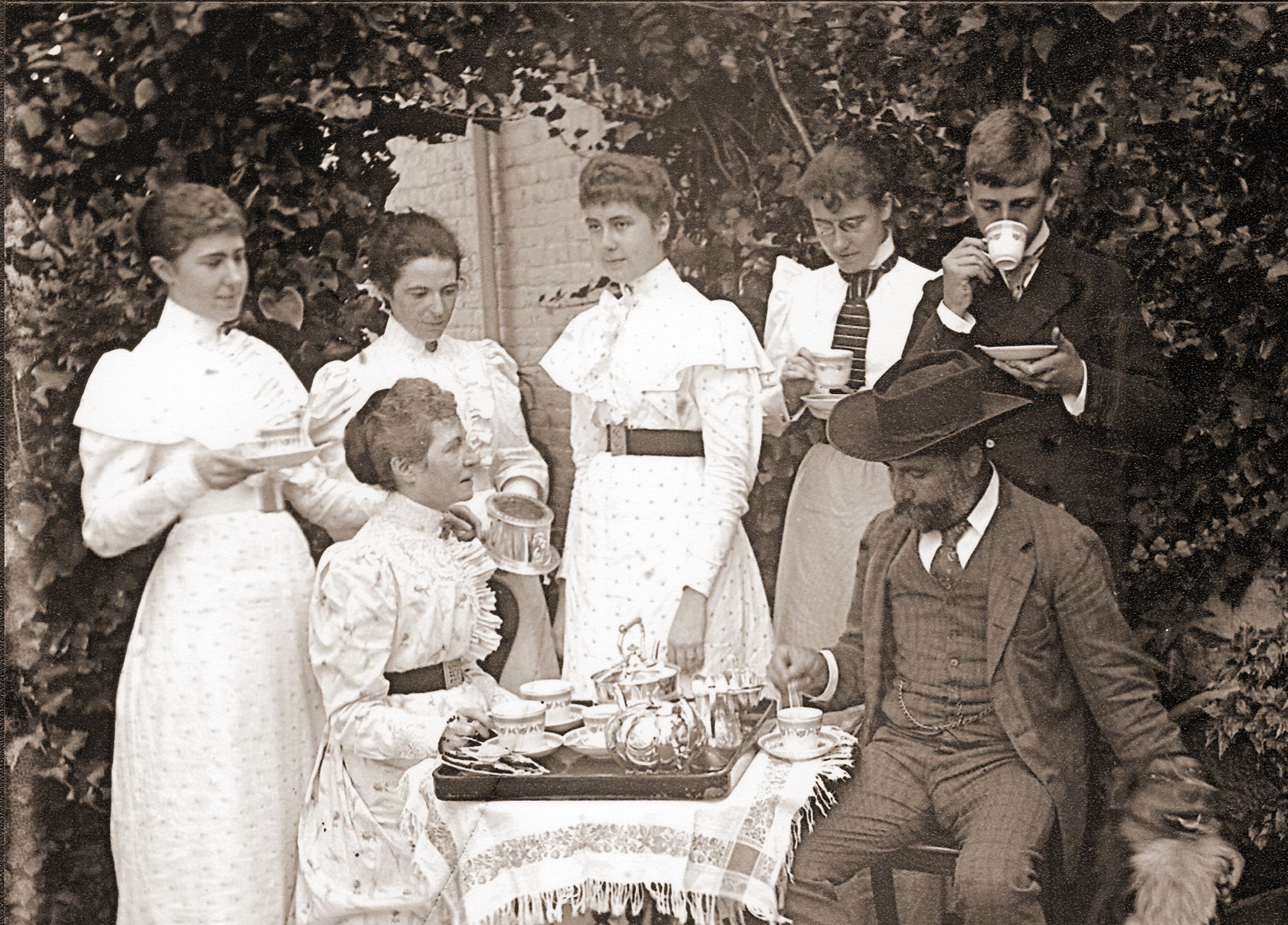 Black and white photograph of people standing around a table drinking tea