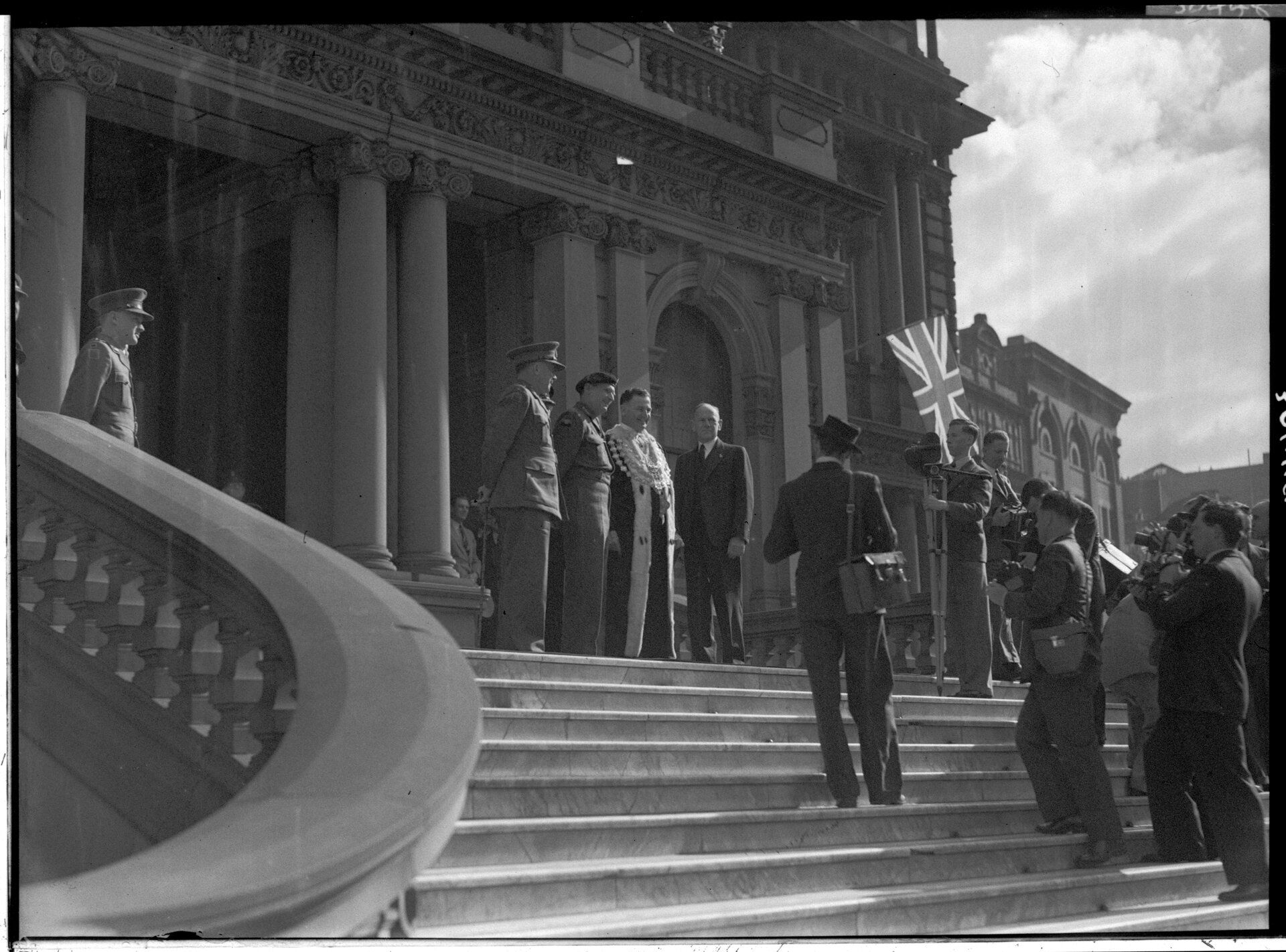 A group of men in uniform and formal attire stand at the top of the stairs to the twon hall