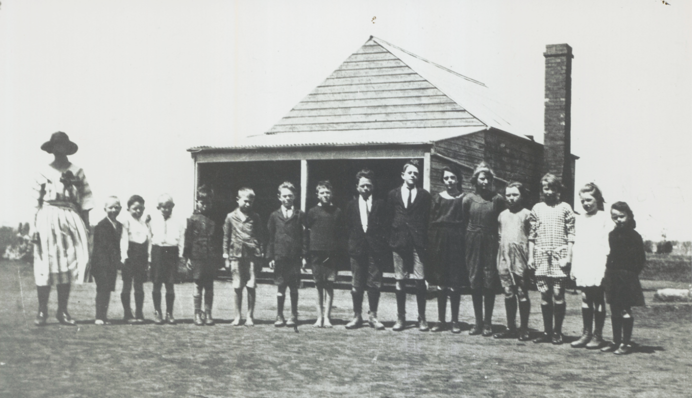 Students and teacher in front of an old school house