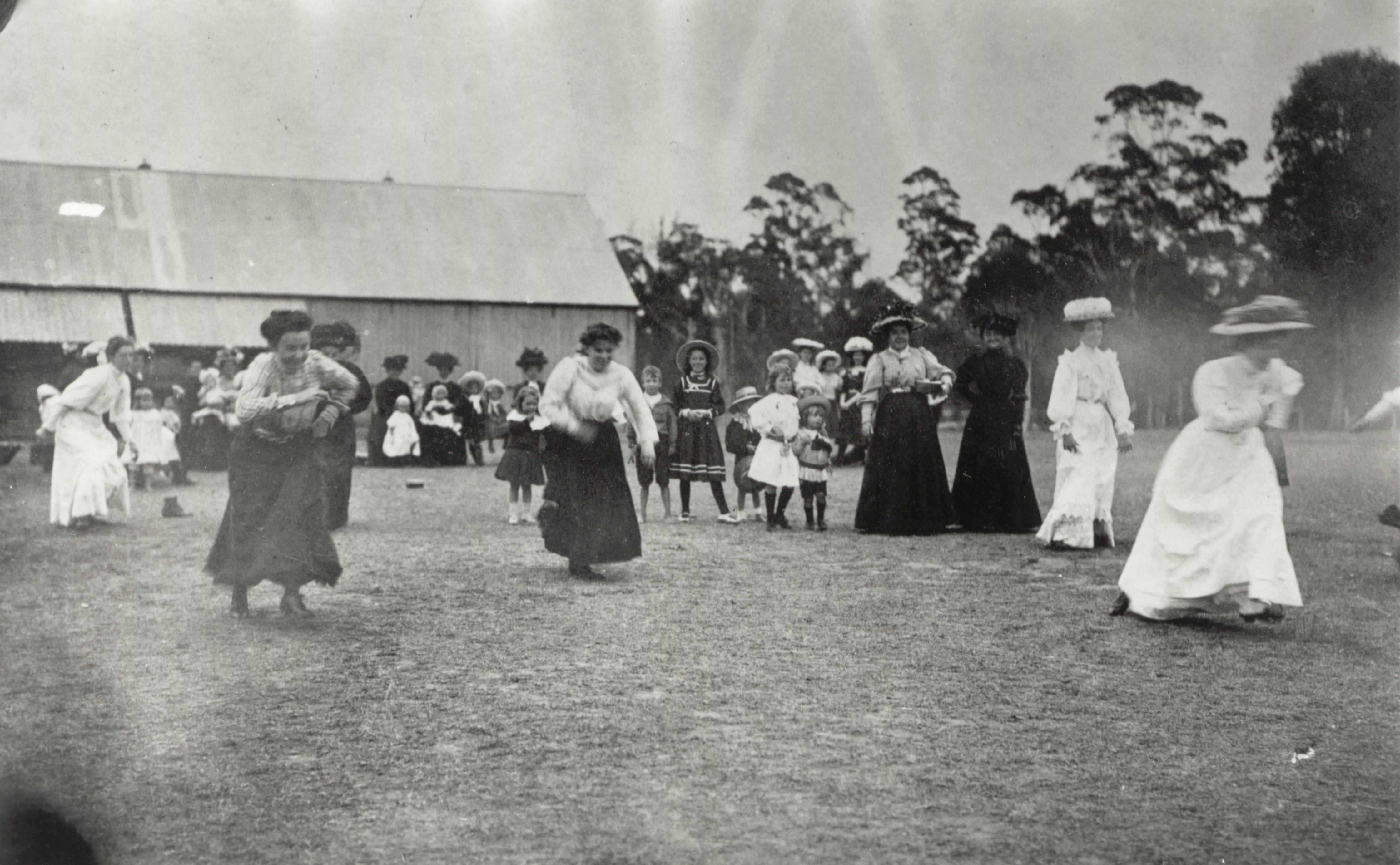 Women in Edwardian fashion running past spectators