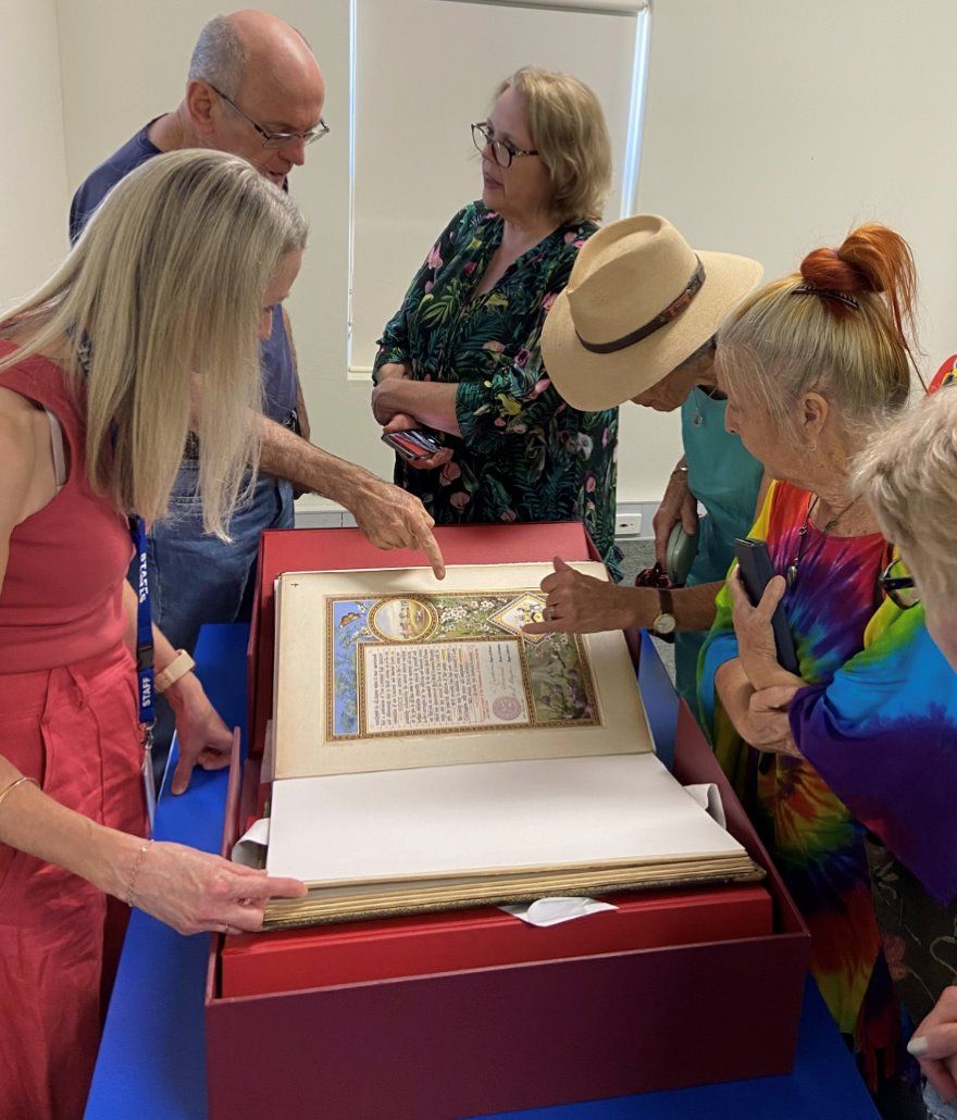 People look at an illuminate manuscript that is supported by a cardboard conservation stand