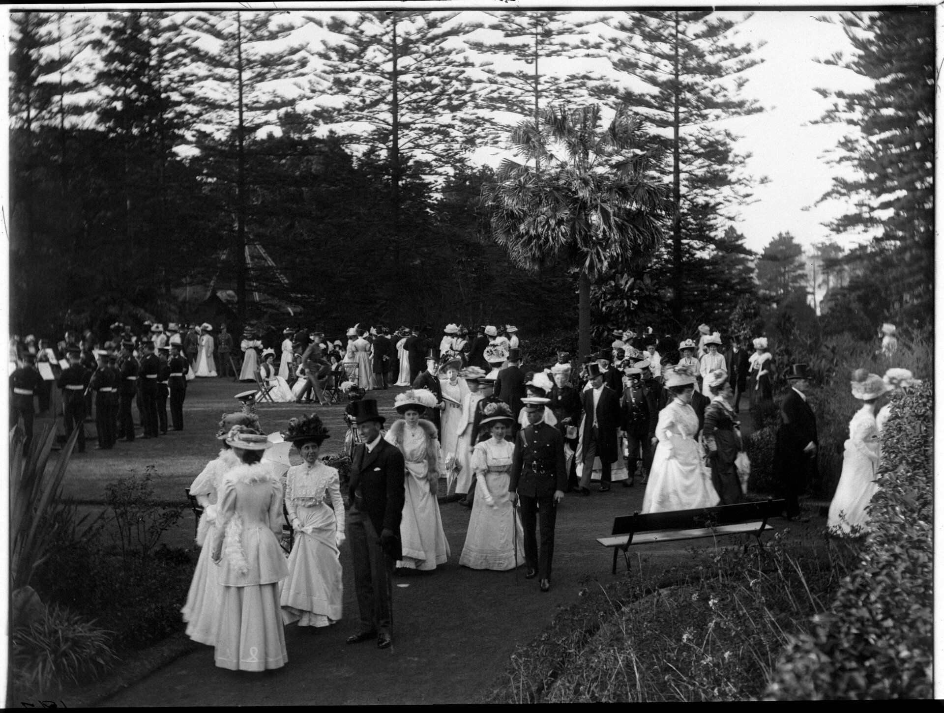 Men and women in formal attire gather outdoors at a garden party