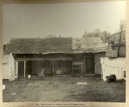  A woman and children sit under the awning of a shed in a muddy yard