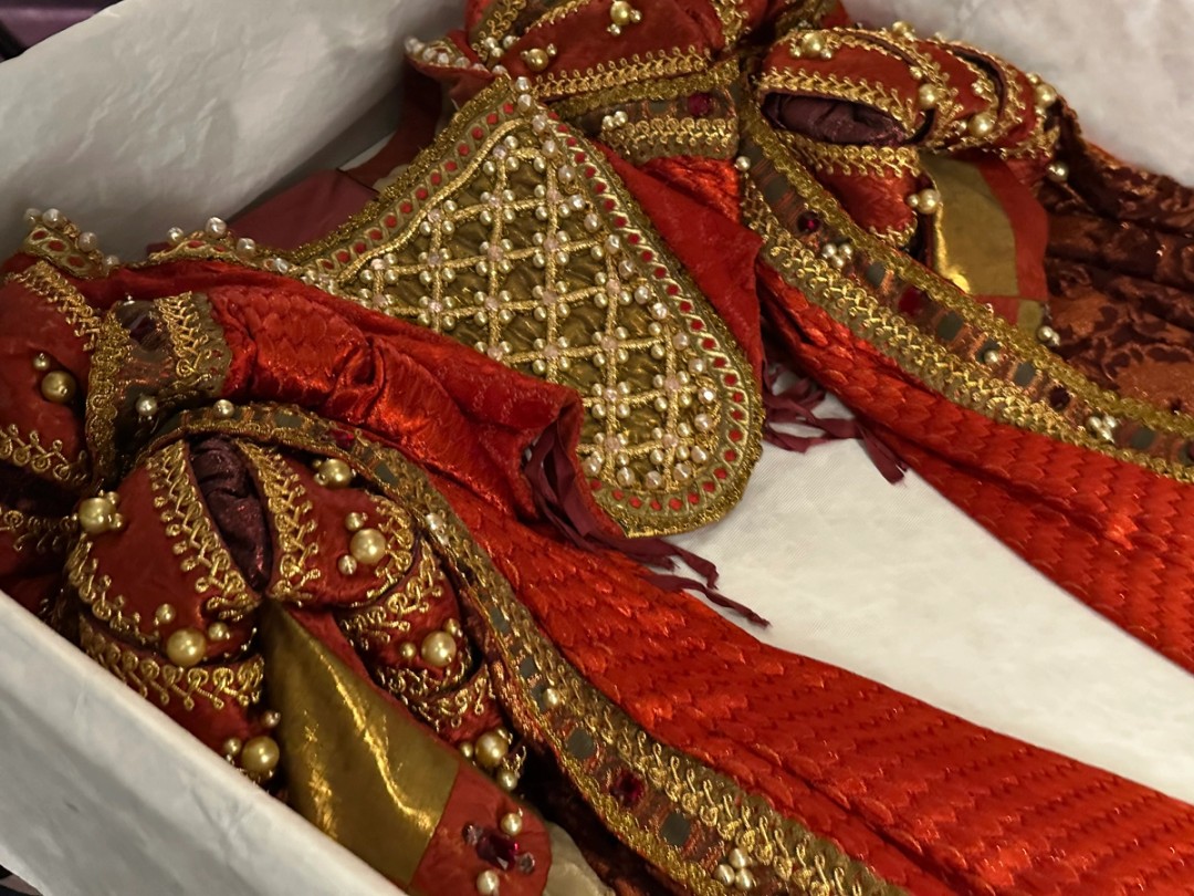 An elaborate sleeved bodice, beaded with faux pearls and with complex appliquéd chest panel and bands in a gold colour, rests in a box.  