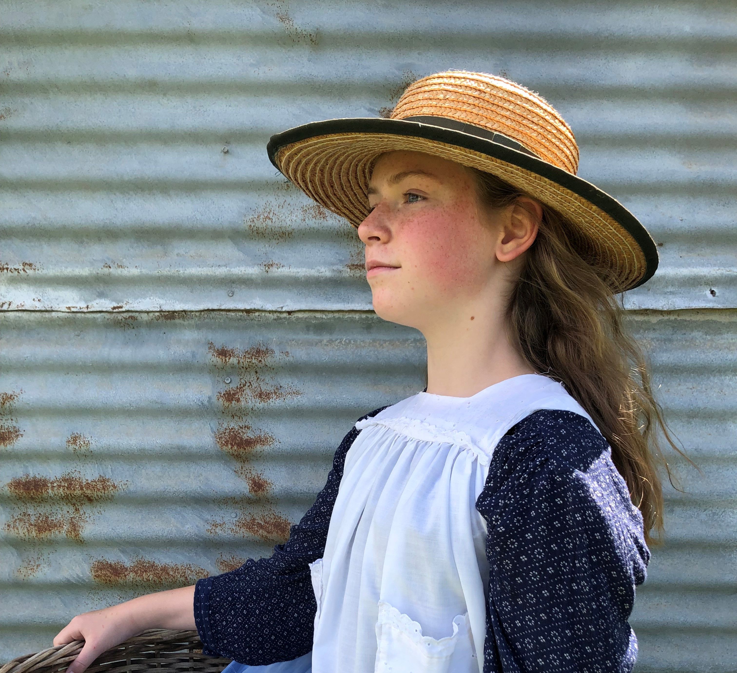 Girl in smock and straw hat holds a basket of laundry