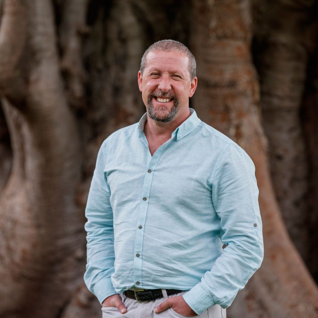 Dave Key wearing a blue shirt standing in front of a large fig tree