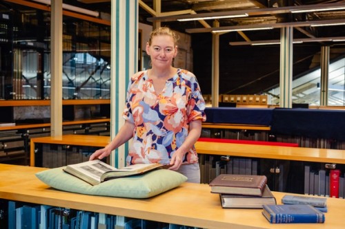 A woman stands at a desk with a library collection placed on a pillow
