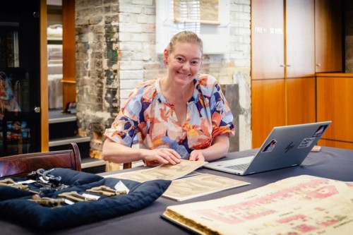 A woman sits in front of a laptop surrounded by archives and objects