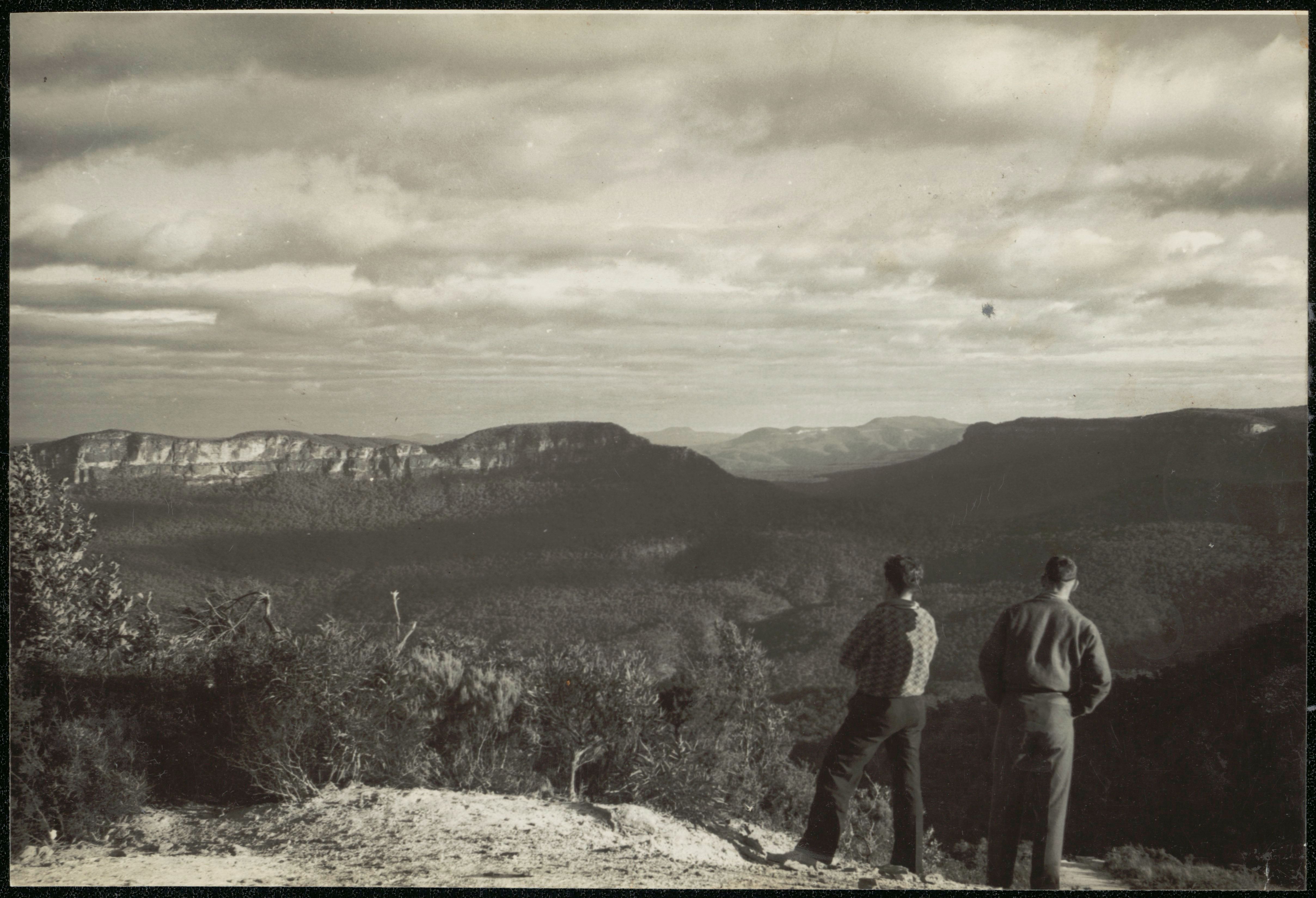 Two men stand at a lookout over a rugged bushland valley