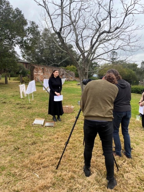 A woman in old fashioned dress stands in front of a film crew