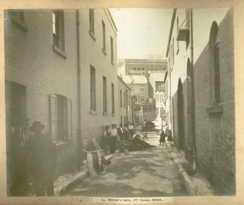 People stand leaning against walls in front of piles of rubbish in a laneway cleansed and swept