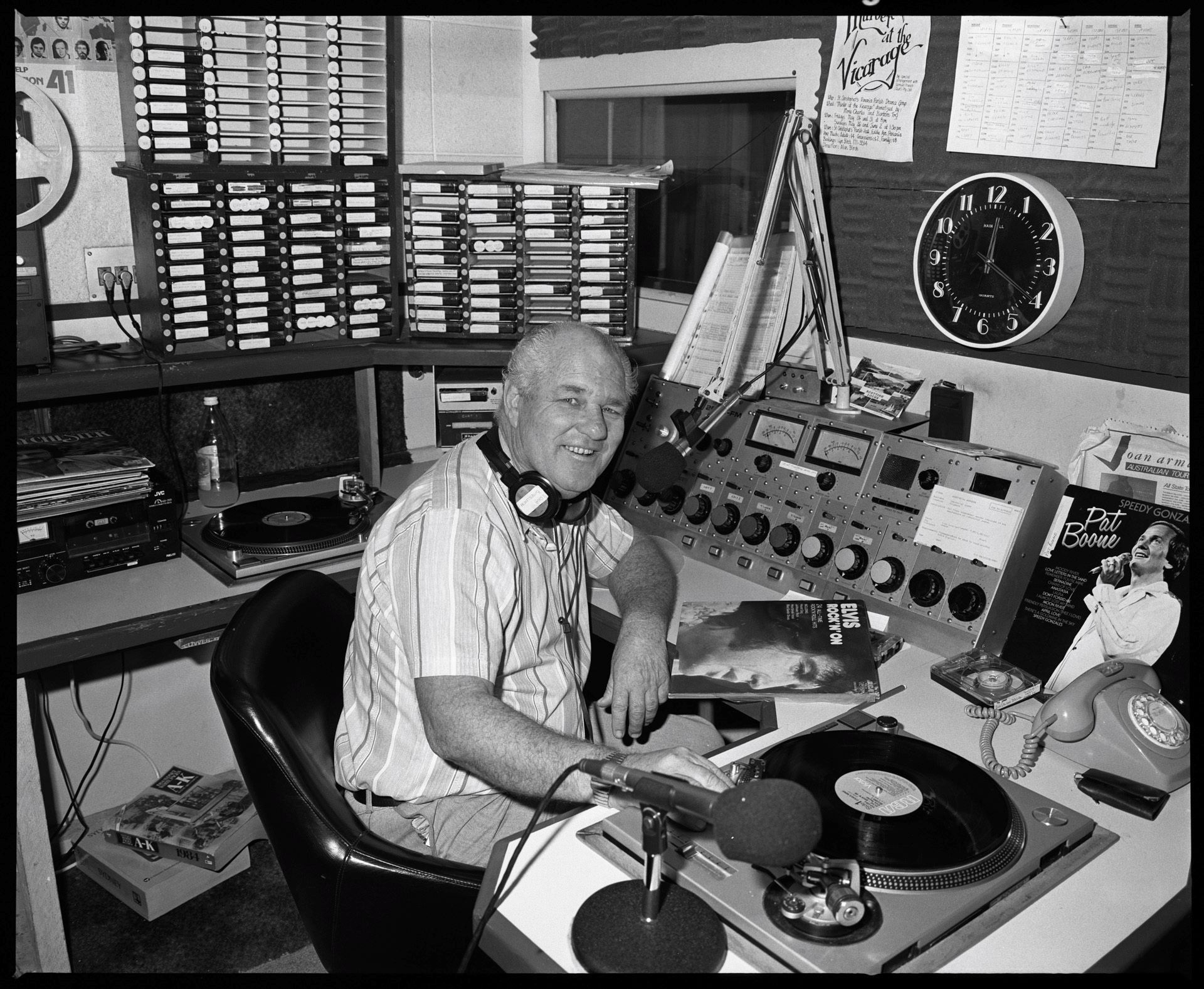 A man with headphones around his neck sits in a radio studio 