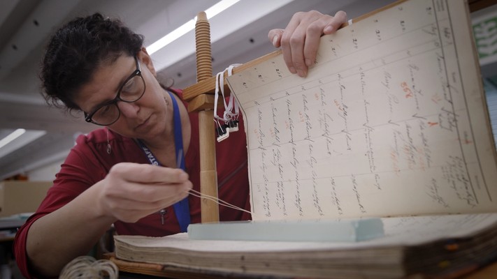 A women holds a large book open while she threads the pages together.