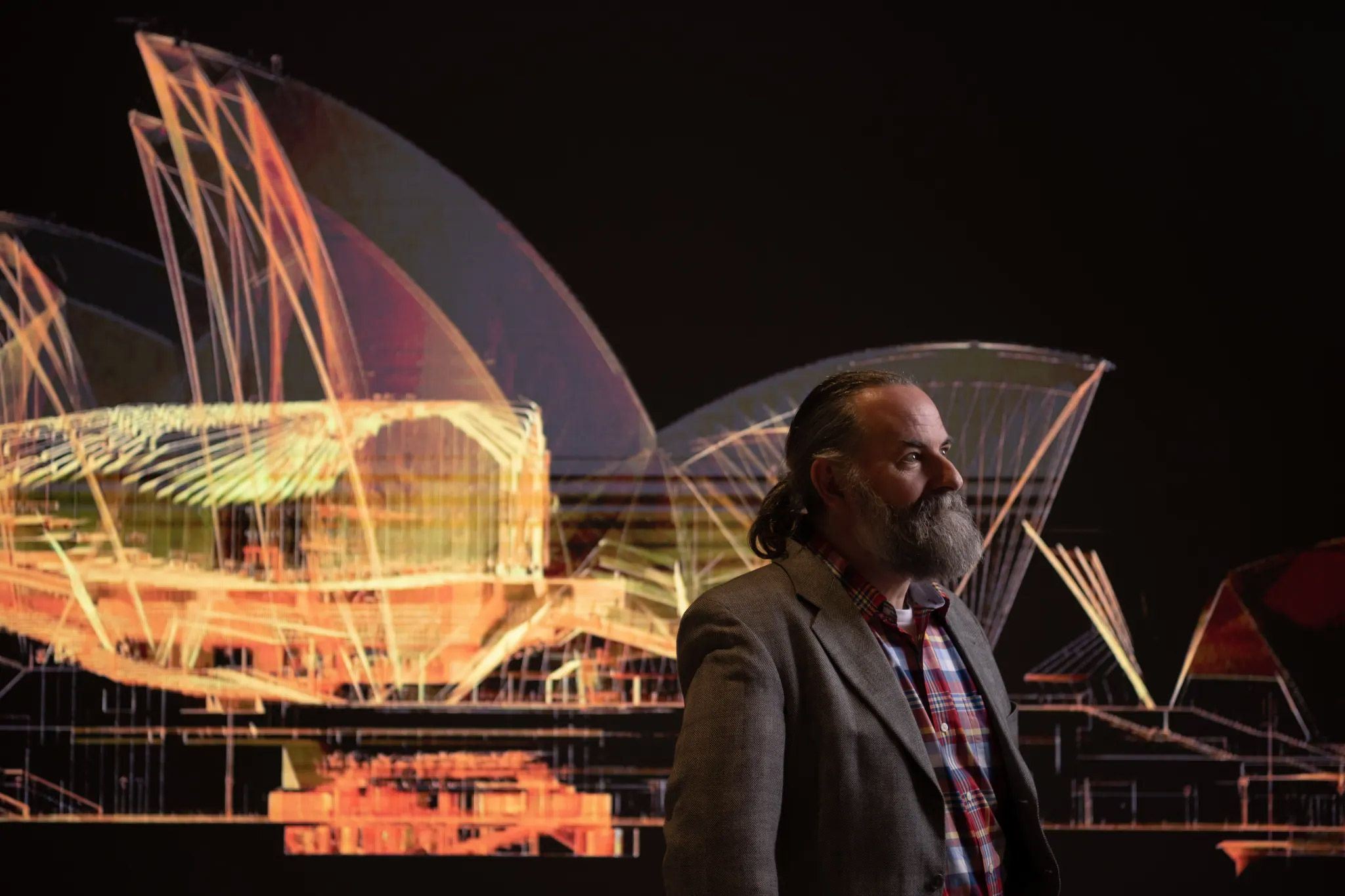 A man standing in profile in front of a digital image of the Sydney Opera House