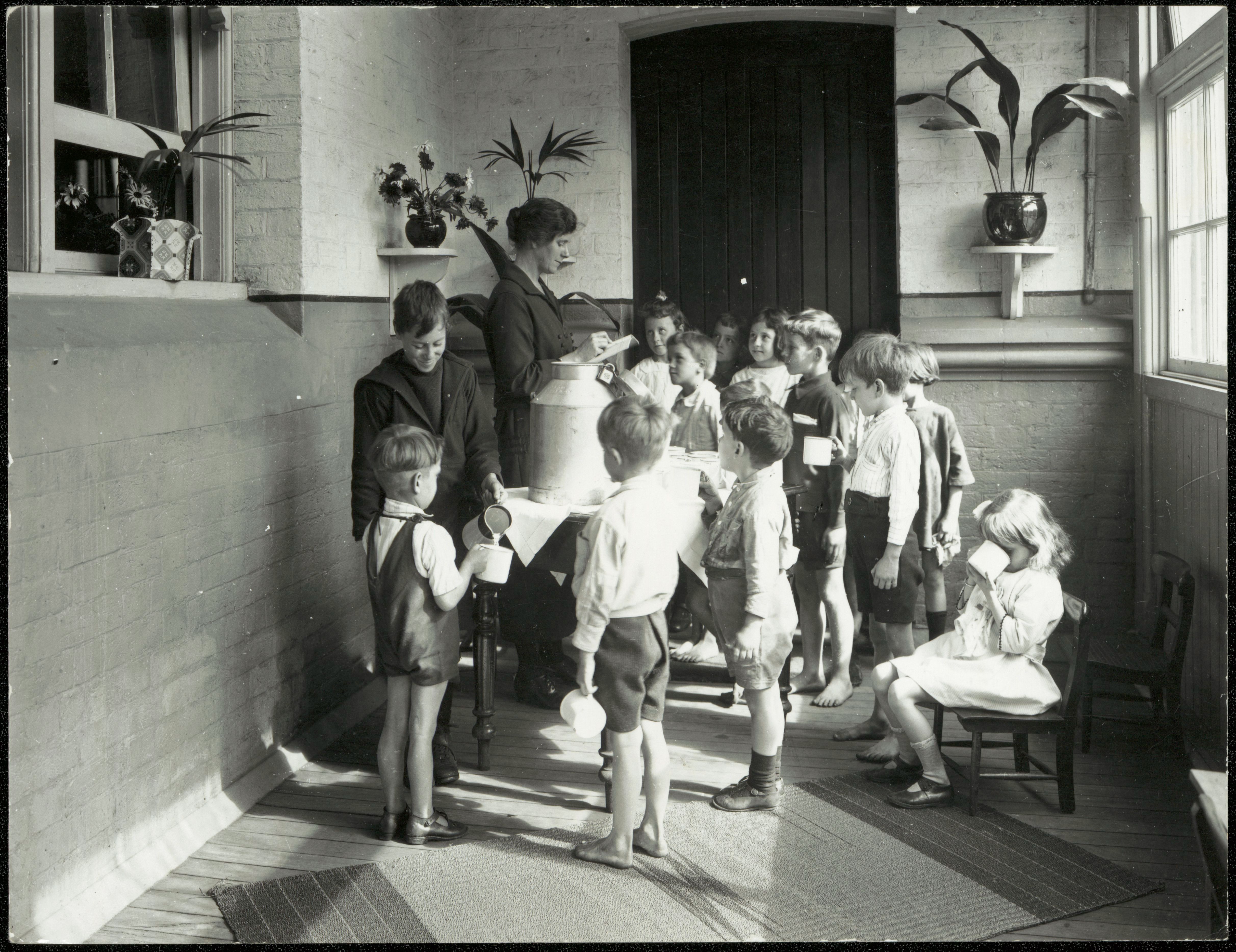  A group of school children wait for their cups to be filled with milk