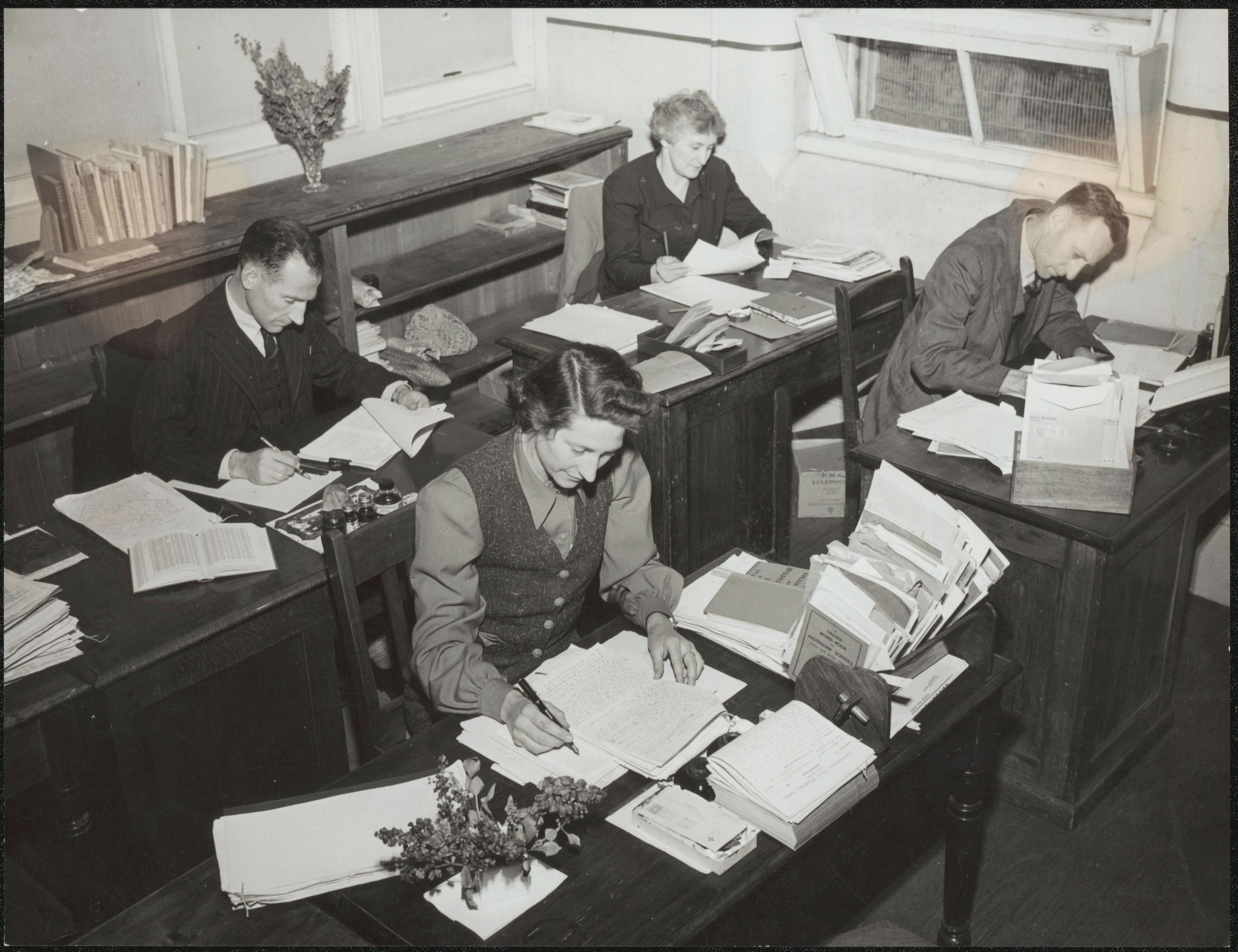 Teachers sit at rows of desk in an office marking schoolwork