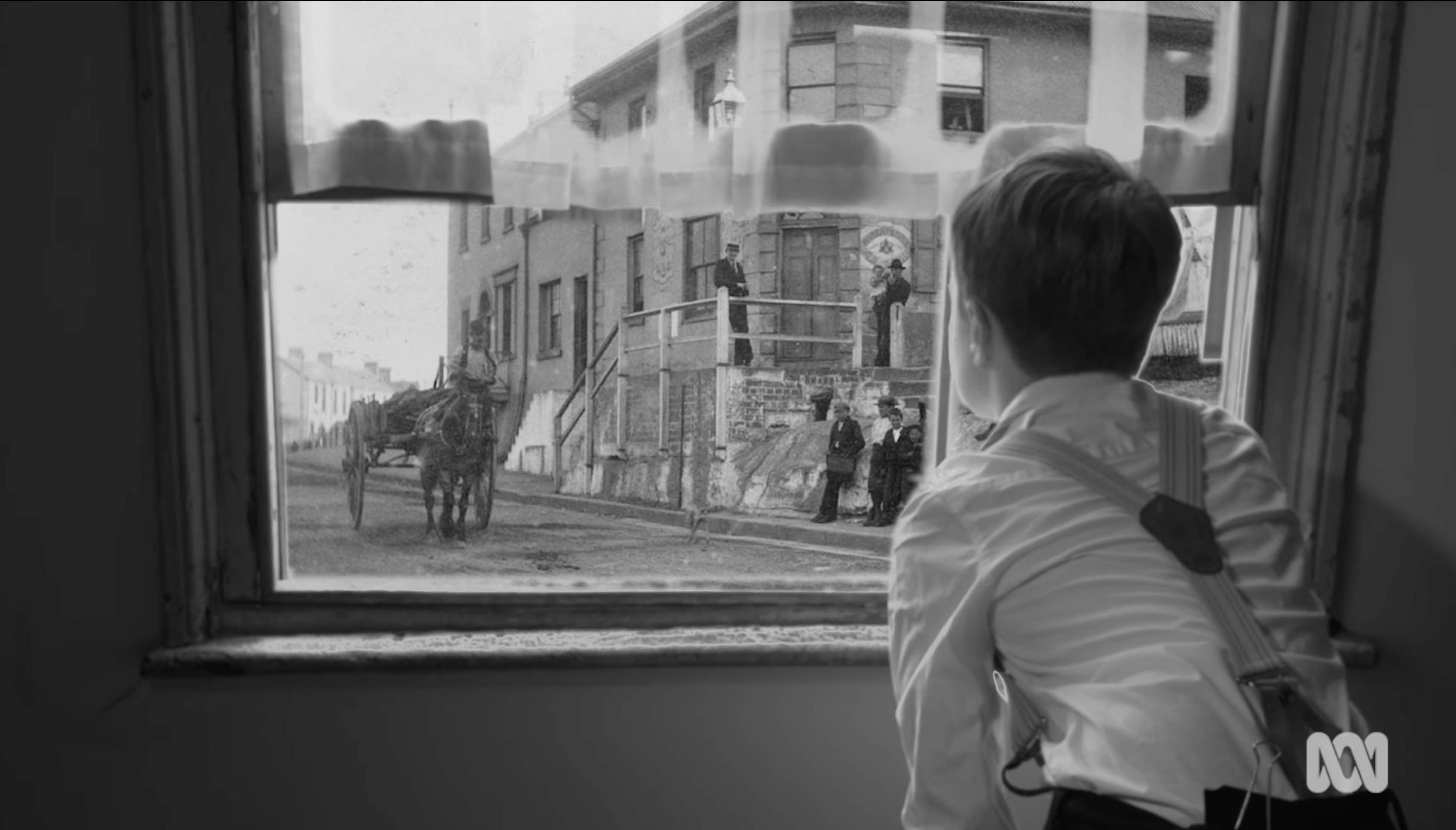 Black and white image of a boy looking out a window