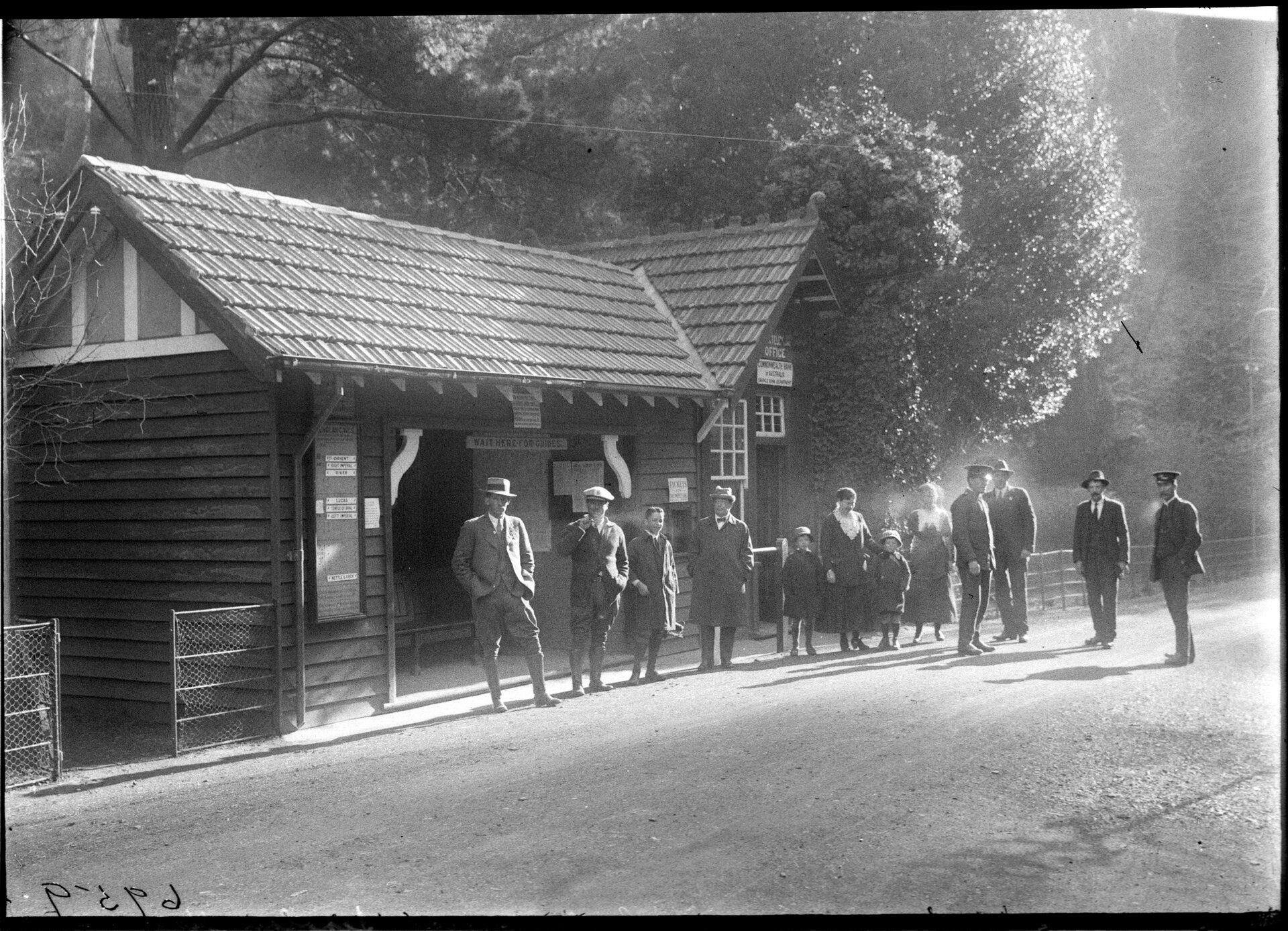 A group of people stand in front of a tourist office. A sign says 'Wait here for guides'