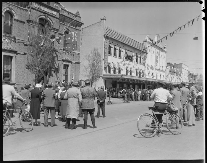 A view from the back of a crowd standing on the main street listening a speaker 