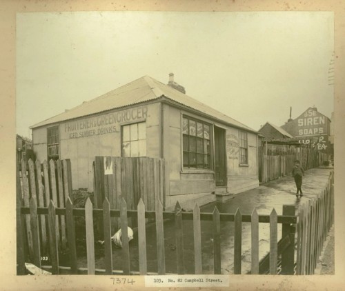 A boy stands on a cleaned footpath outside a fruiterer and green grocer