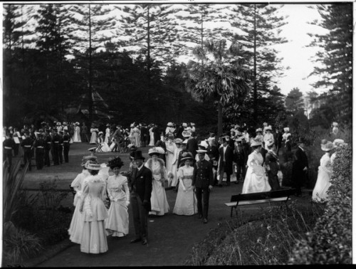 Men and women in formal attire gather outdoors at a garden party