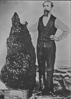 Man standing next to the largest reef gold nugget ever discovered in the world. The nugget is 144.8cm