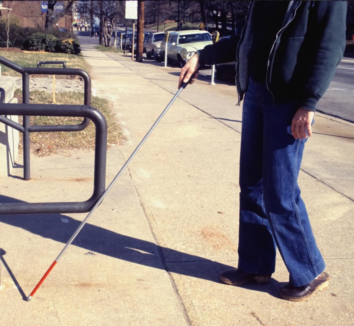 a person using a mobility cane walking on a concrete sidewalk