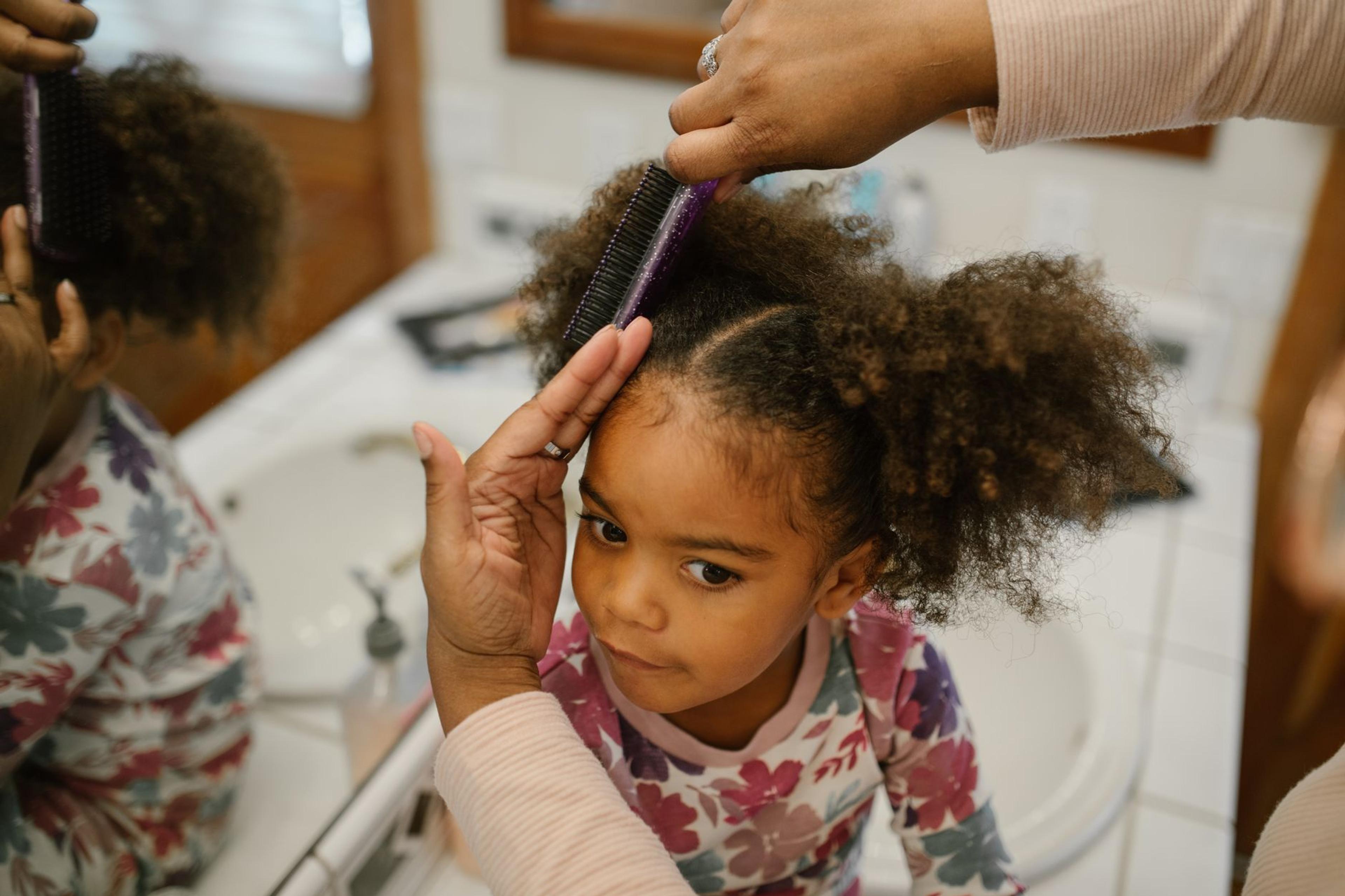A parent gently detangling their child's textured curly hair using a spray, creating a nurturing hair care routine