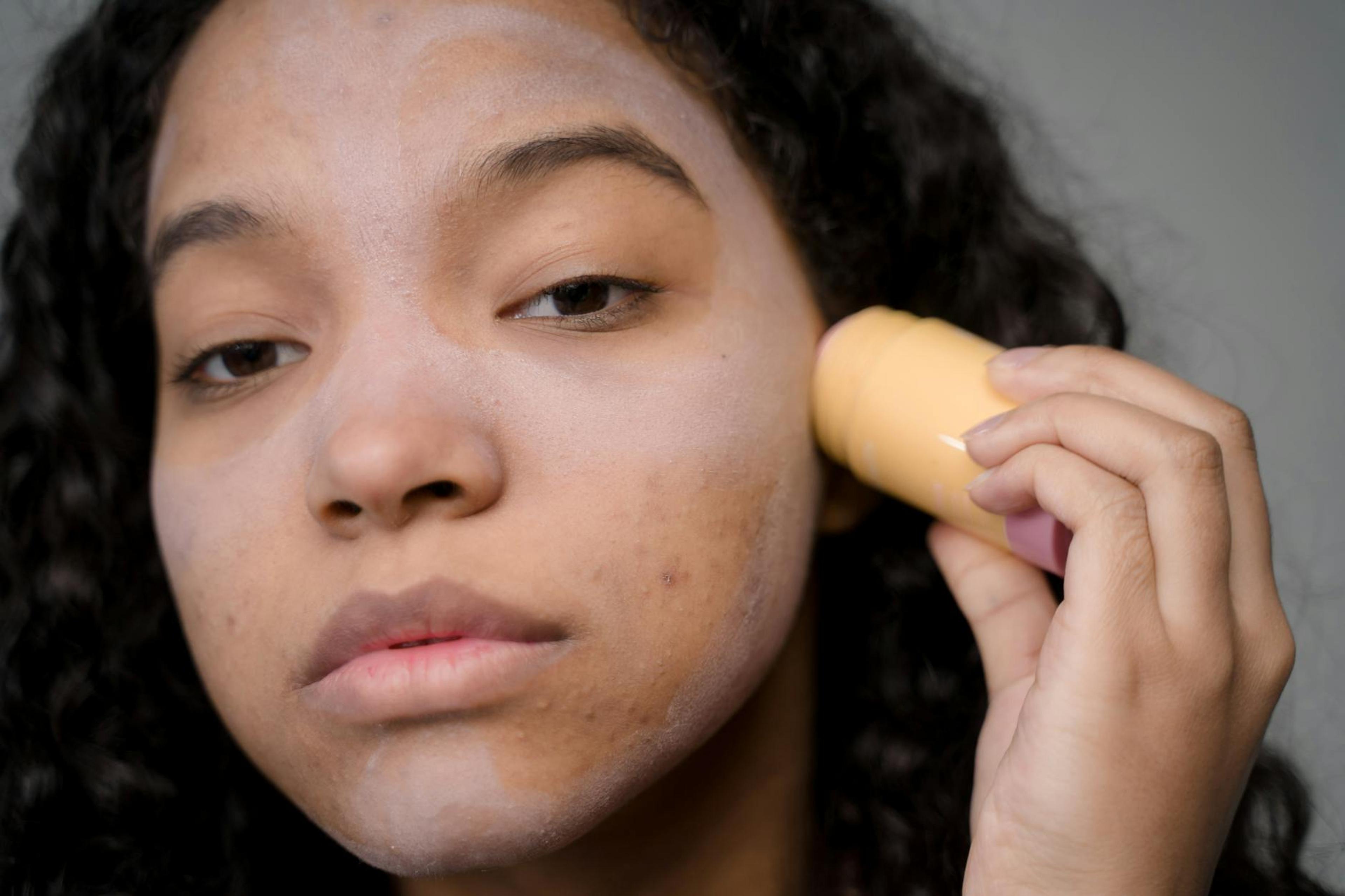A black woman with textured natural hair applying skincare products to her face in a bright, well-lit setting, showcasing her glowing skin and confidence.