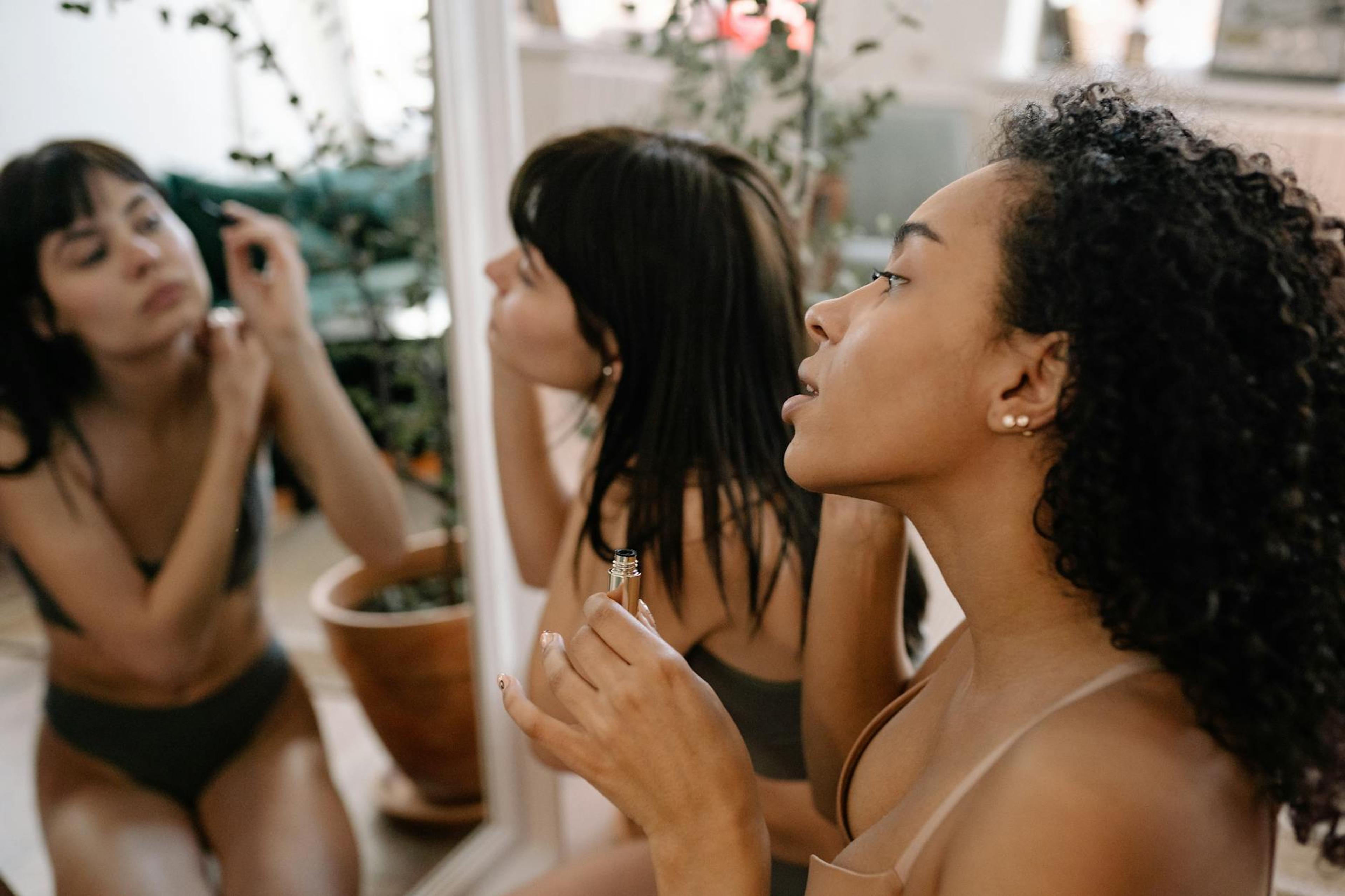 A Black woman with textured natural hair applying niacinamide serum to her face in a well-lit, professional setting, showcasing her healthy, glowing skin.