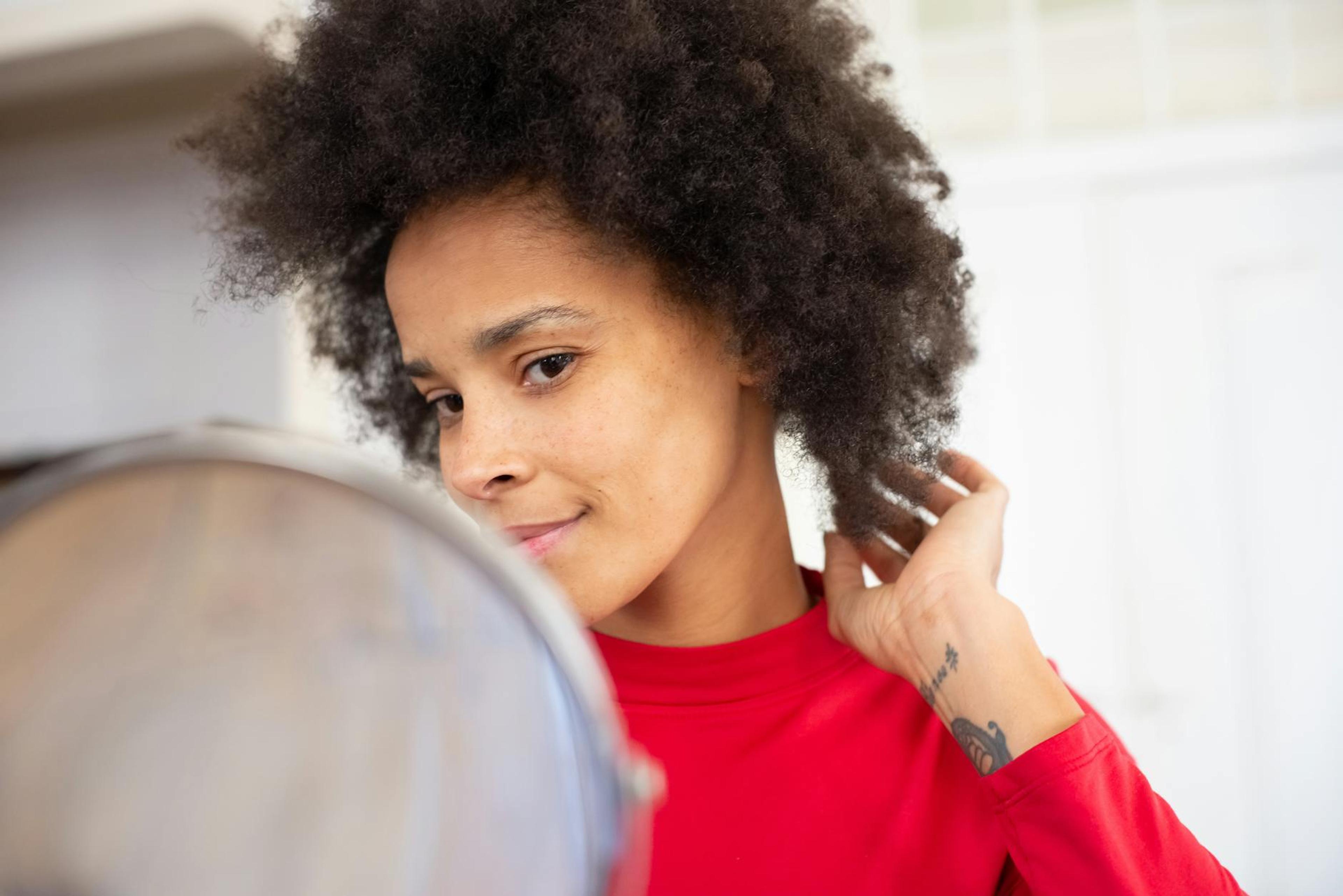 A Black woman with beautiful, well-defined curls applying a moisturizing product in a well-lit bathroom, showcasing a nurturing hair care routine.