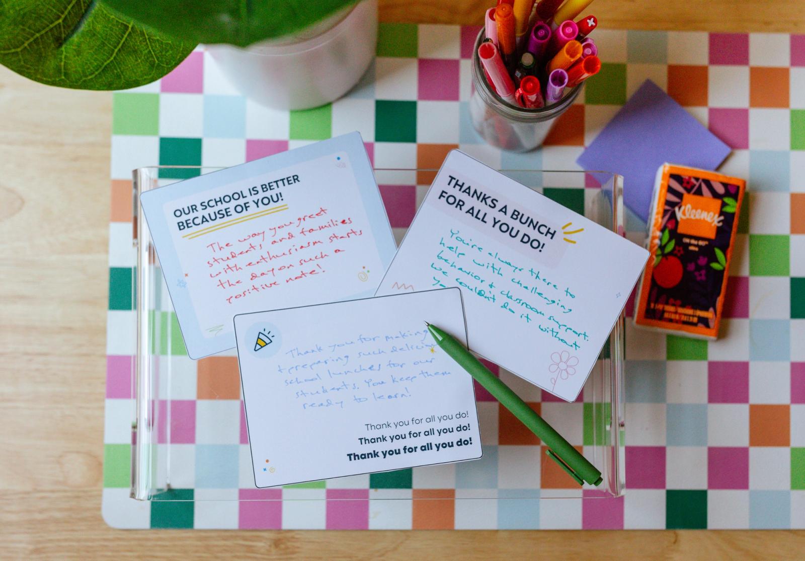 Three handwritten notes lay on a desk with a colorful checkered placemat on it. 
