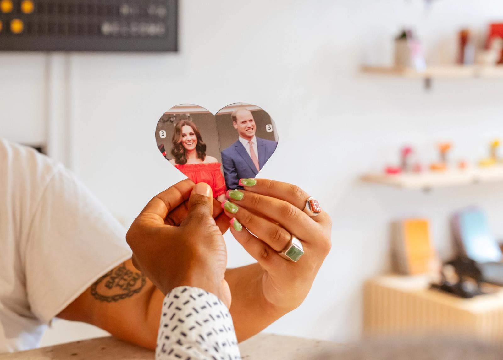 Two hands hold together two halves of a heart with celebrity images on them. 