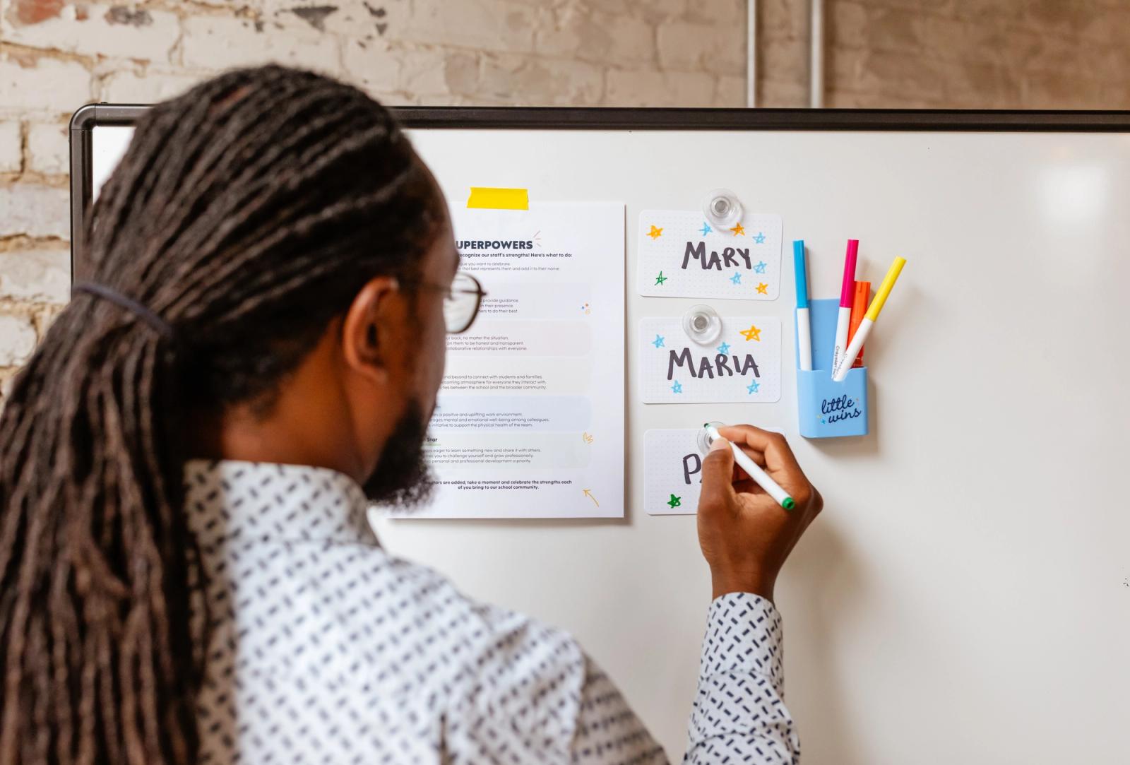 A man stands at a whiteboard writing on notecards with peoples' names on them.