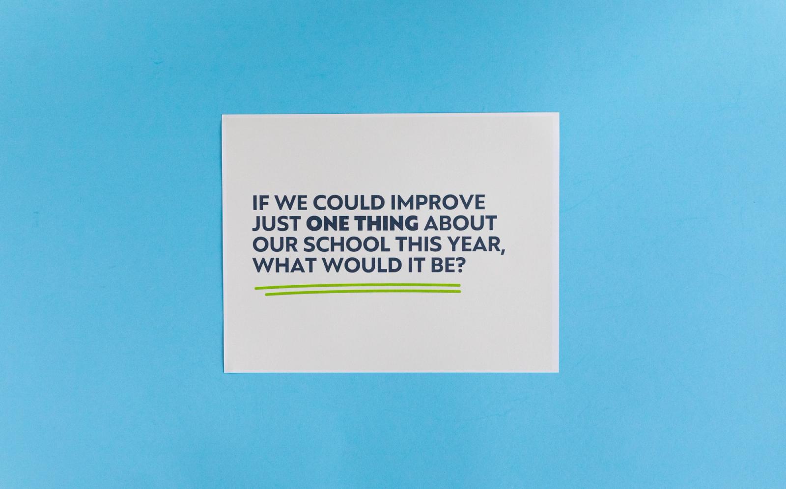 Sheet of paper that says "if we could improve just one thing about our school this year, what would it be?" lays on a light blue background.