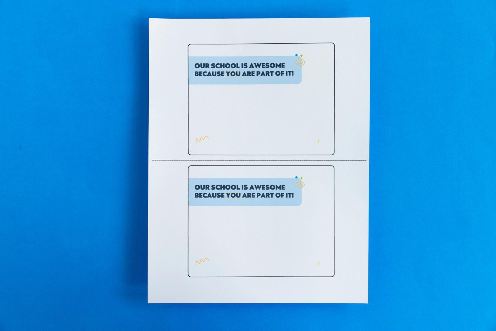 A piece of paper that has two notecards on it that say "our school is awesome because you are part of it" lay on a blue background.